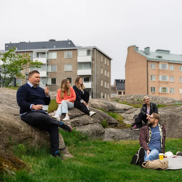 Six members of the MinnaLearn team sitting on rocks and grass in front of apartment buildings