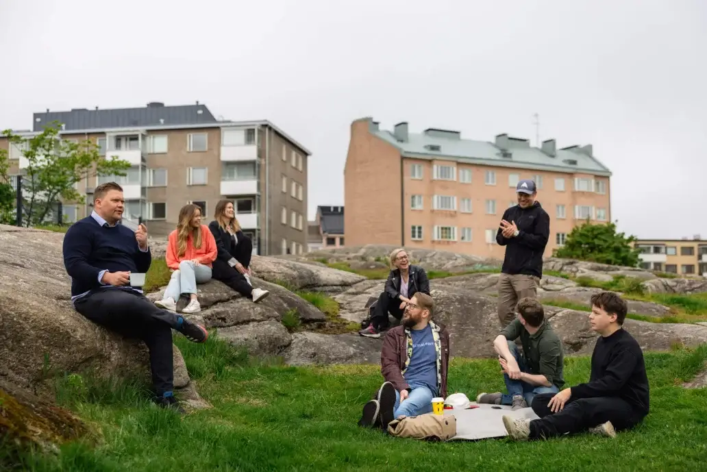 Five people chatting and relaxing on grass and rocks in front of apartment buildings