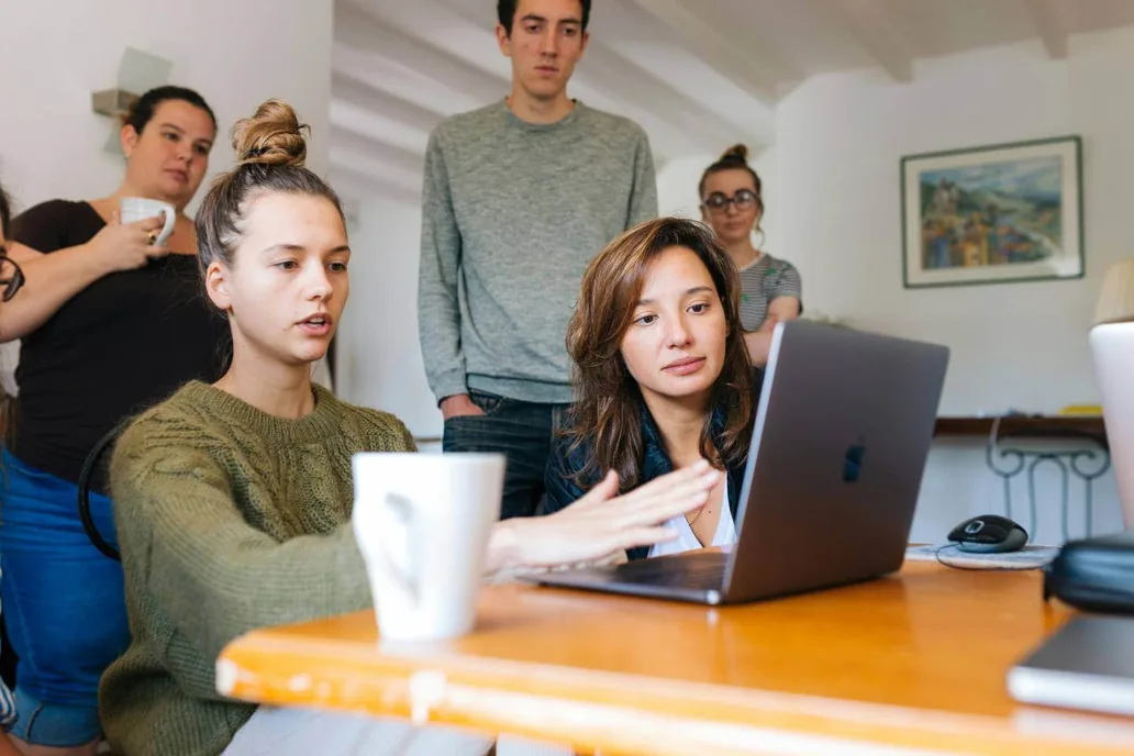 Colleagues gathered around a laptop in an office, discussing what is on the screen